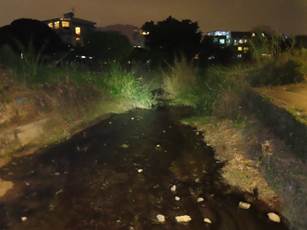 A dark muddy path with buildings in the background

Description automatically generated